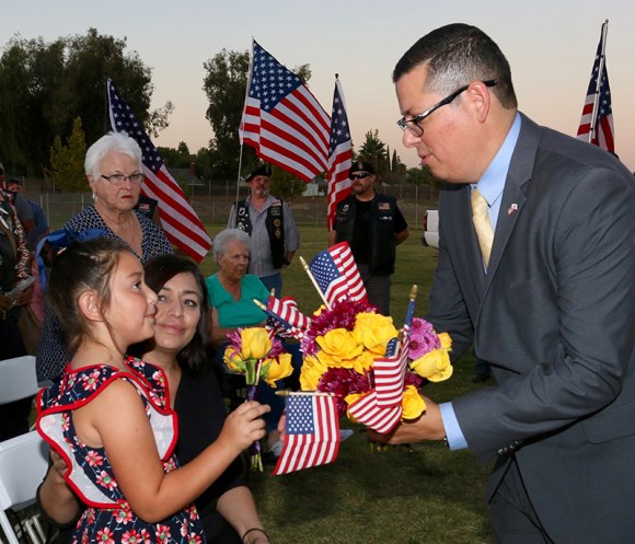 Kings County's assemblyman, Rudy Salas, hands flowers and flags to Gold Star families during a tree-planting ceremony Friday at Kings LIons Park.